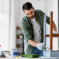 Person painting a wooden chair with a brush.